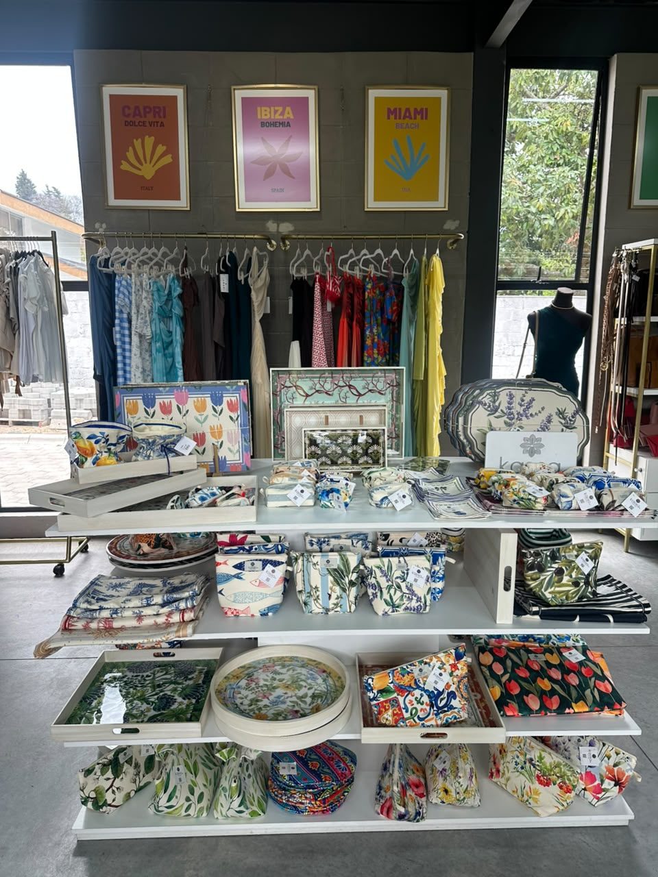 Mesa de exhibición con mantelería, individuales estampados, bandejas y vajilla, bajo tres láminas enmarcadas de colores