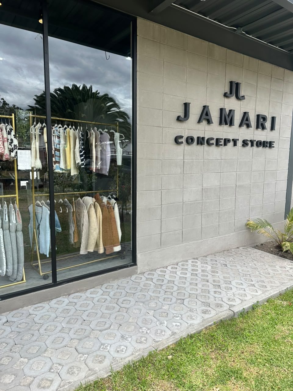 Fachada de Jamari Concept Store: el letrero JAMARI CONCEPT STORE sobre el muro de bloque y la vitrina con perchas de ropa de mujer