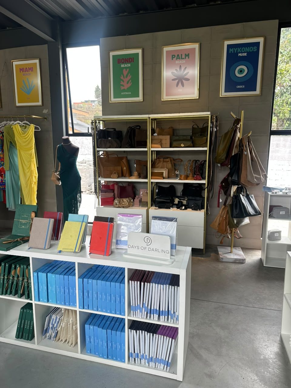 Mesa de papelería con planners y cuadernos de Days of Darling, y al fondo estanterías de carteras y bolsos de cuero