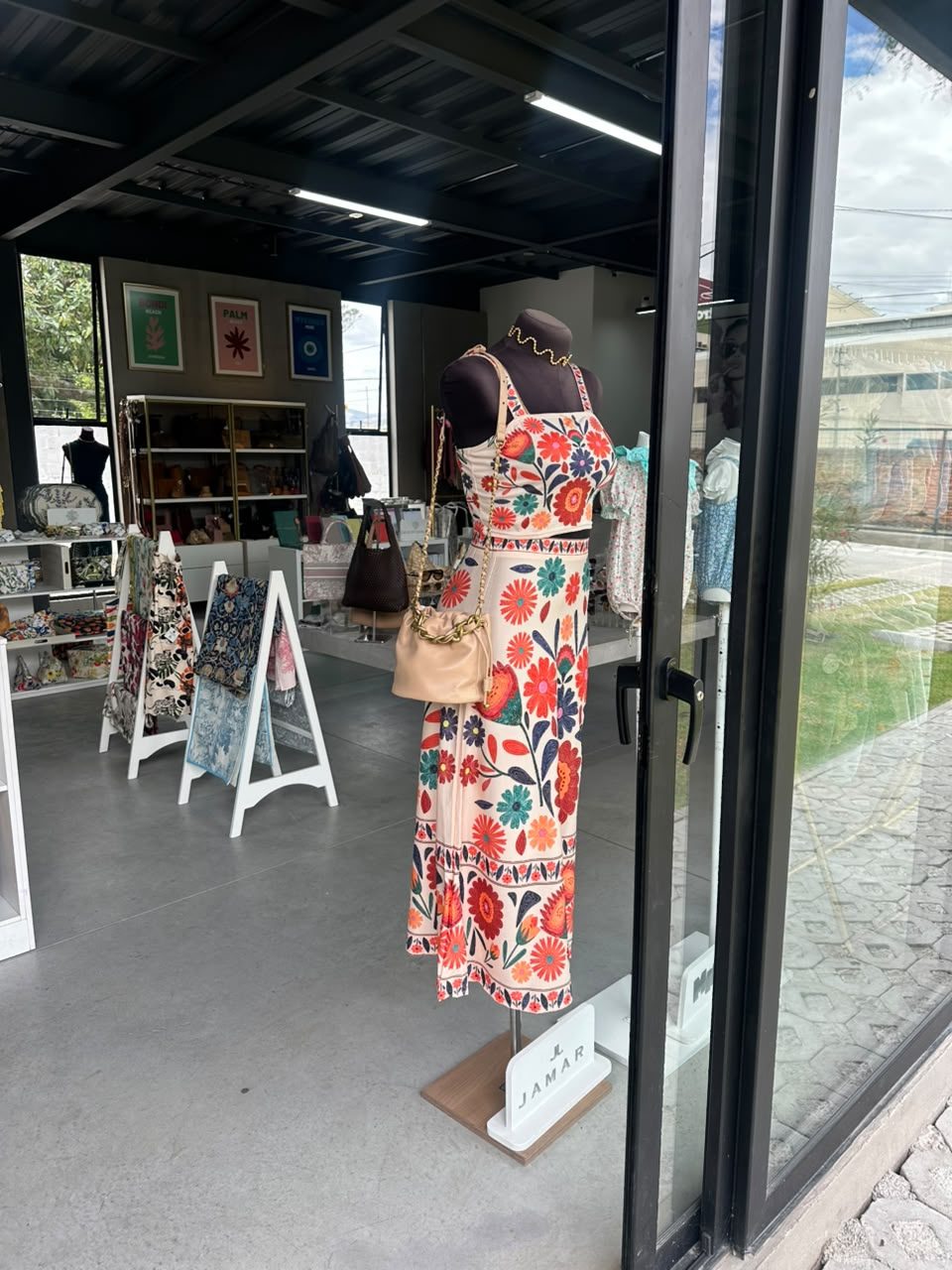Maniquí en la entrada de la tienda con un vestido largo de estampado floral y una cartera de cuero colgada al hombro
